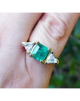 Women's ring with a center natural colombian emerald and two trillion side diamonds, crafted in 18k yellow gold.