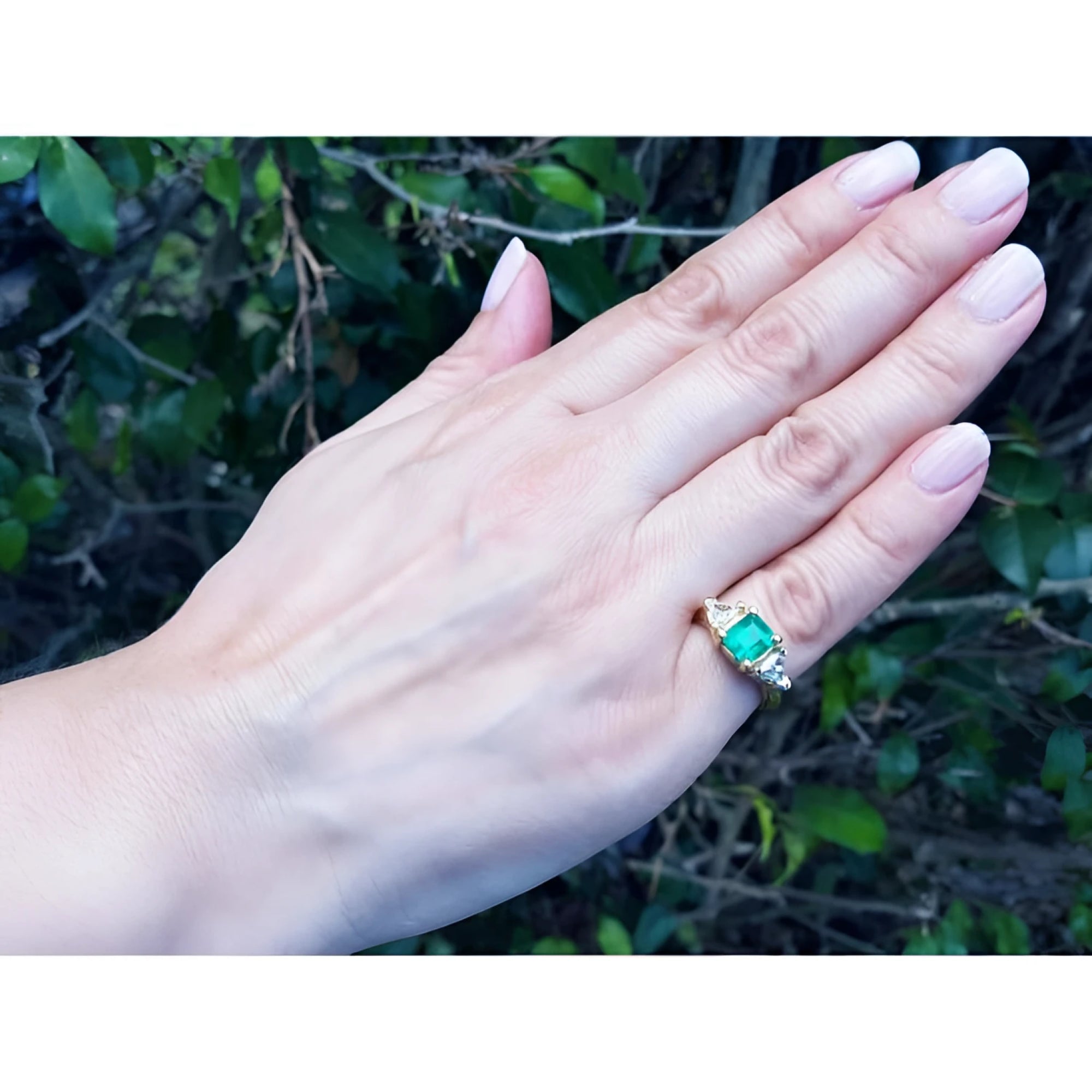 1.47 ct. emerald-cut Colombian emerald ring with trillion diamonds in 18k yellow gold on a hand.