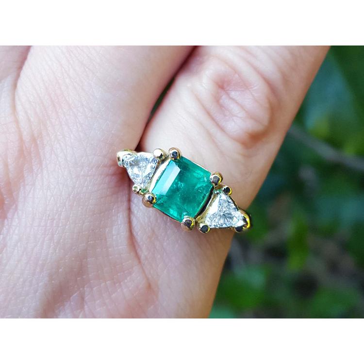 Women's ring with a center natural colombian emerald and two trillion side diamonds, crafted in 18k yellow gold.
