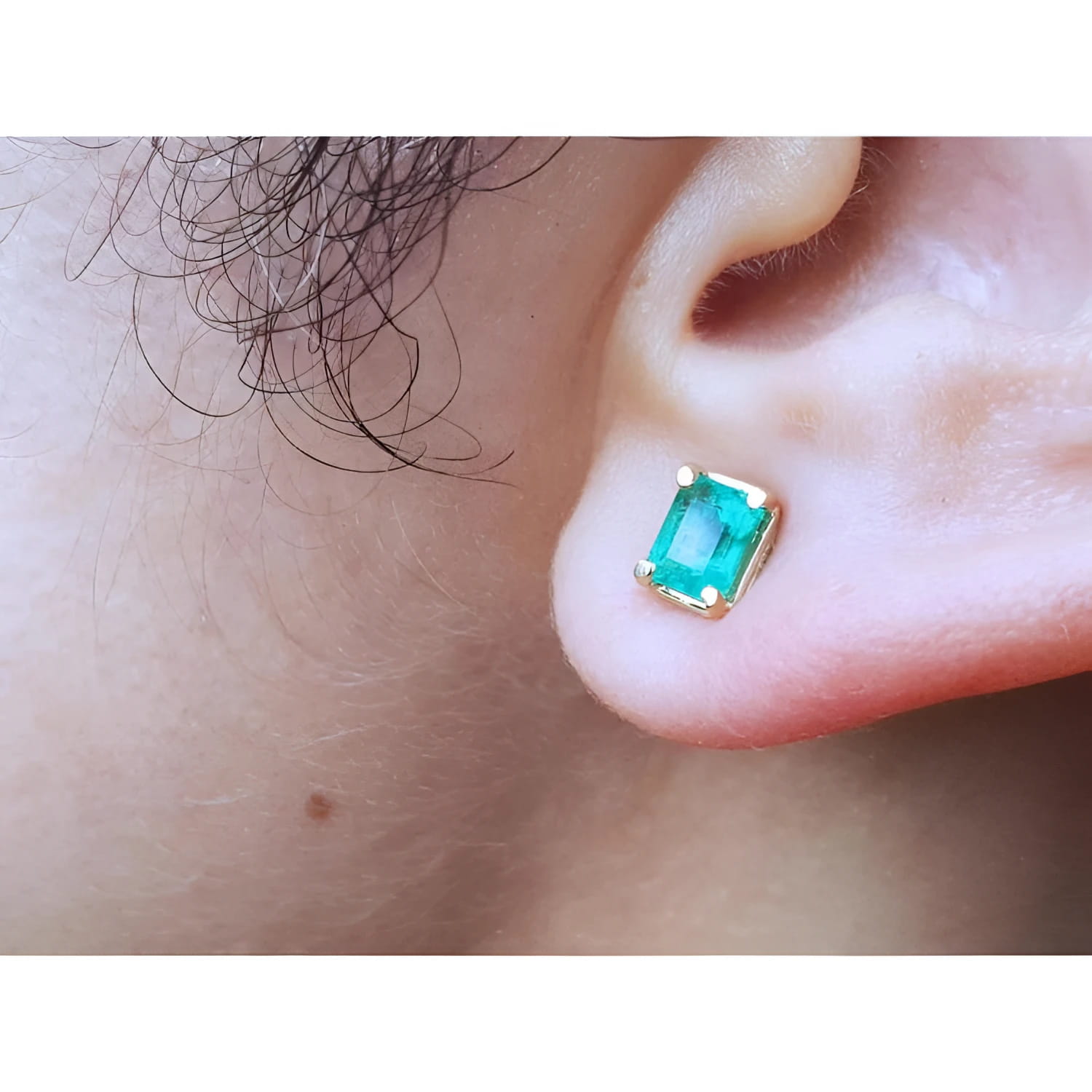 An earlobe wearing a natural colombian emerald stud earring in 14k yellow gold.