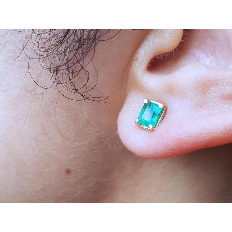 An earlobe wearing a natural colombian emerald stud earring in 14k yellow gold.