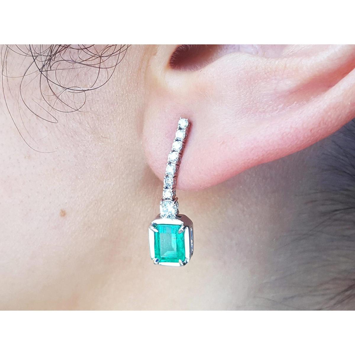 Close-up of an emerald dangle earring on a person's ear.