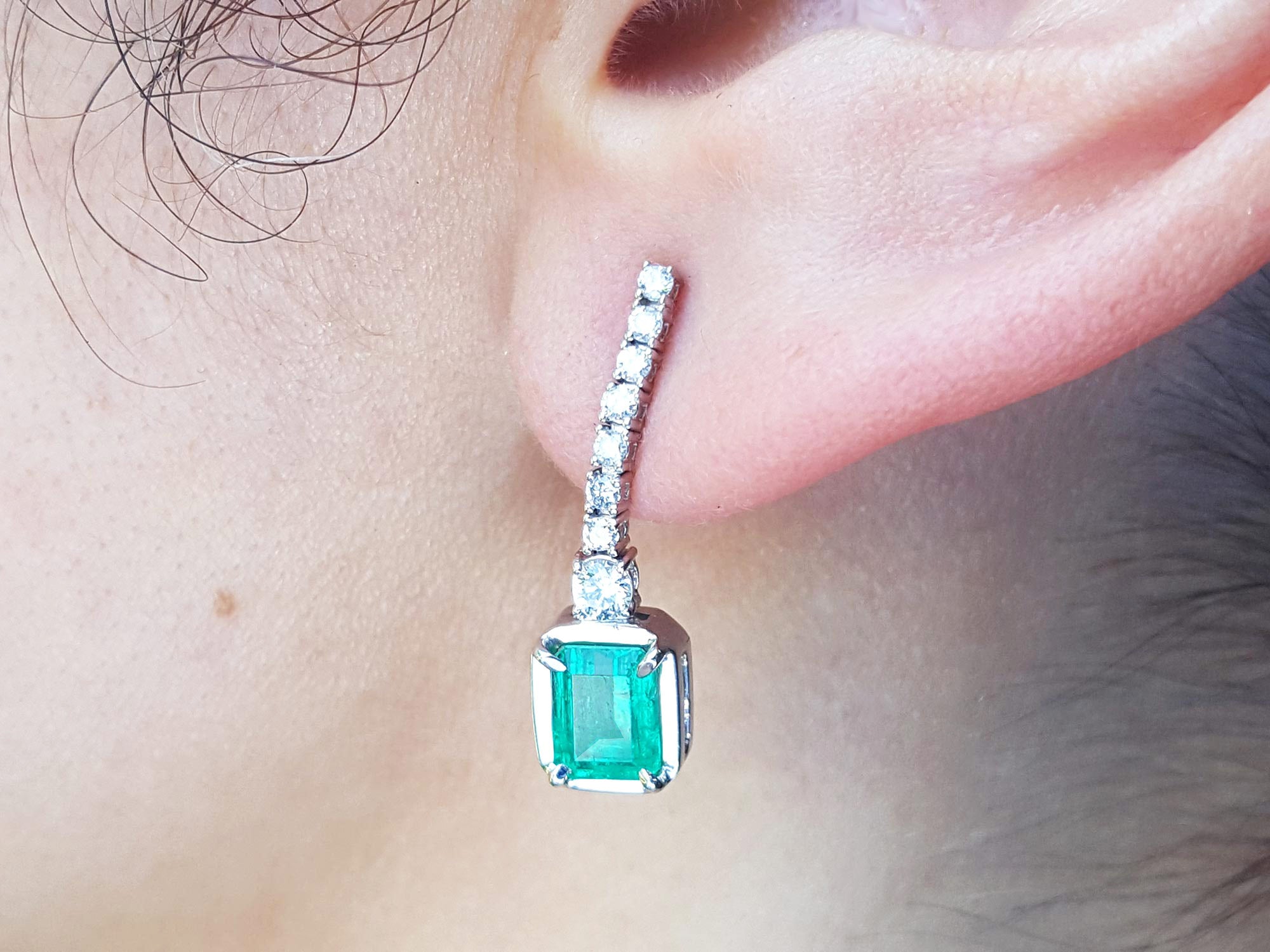 Close-up of an emerald dangle earring on a person's ear.
