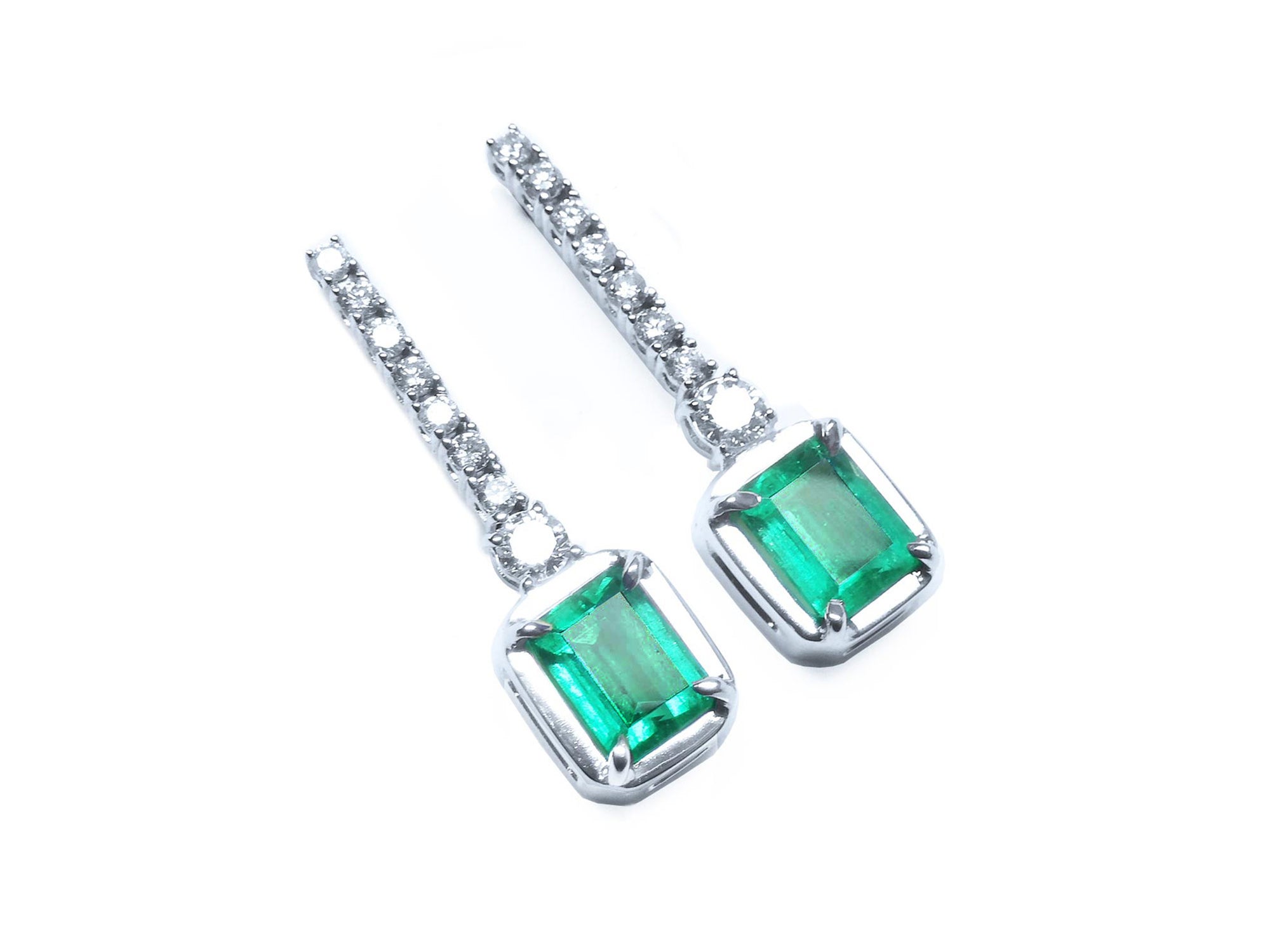 Pair of emerald dangle earrings with 14k white gold settings right side position top view