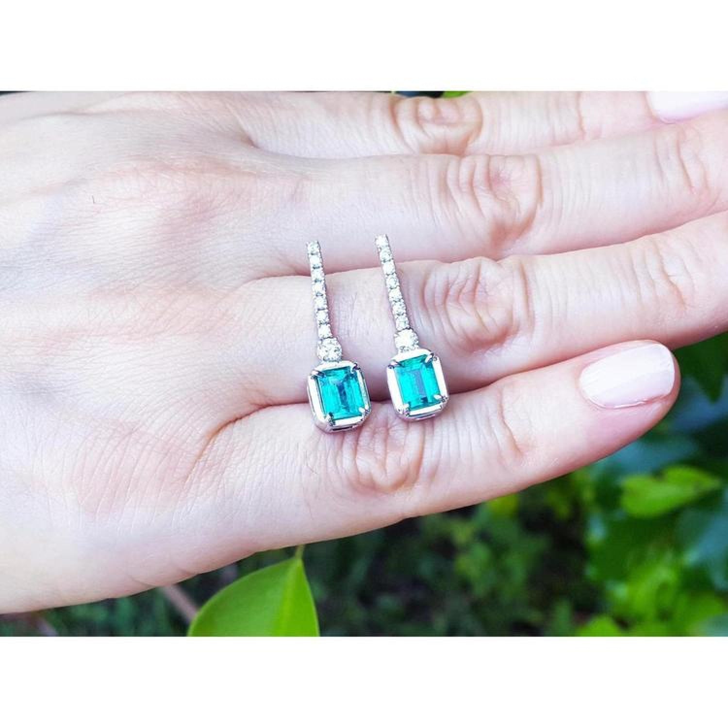 18K white gold dangling emerald-cut emerald earrings with diamond-studded lines.