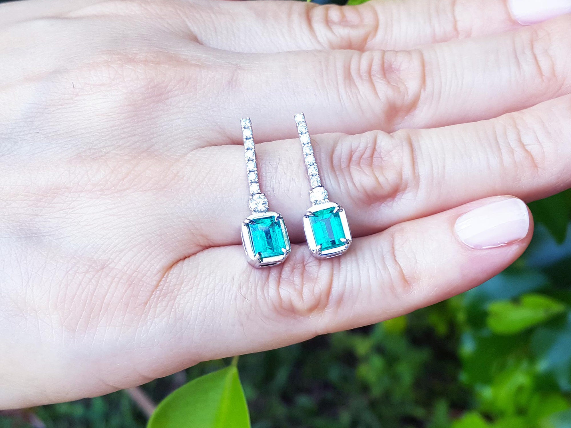 Pair of emerald-cut gemstone earrings held in a hand with a natural background
