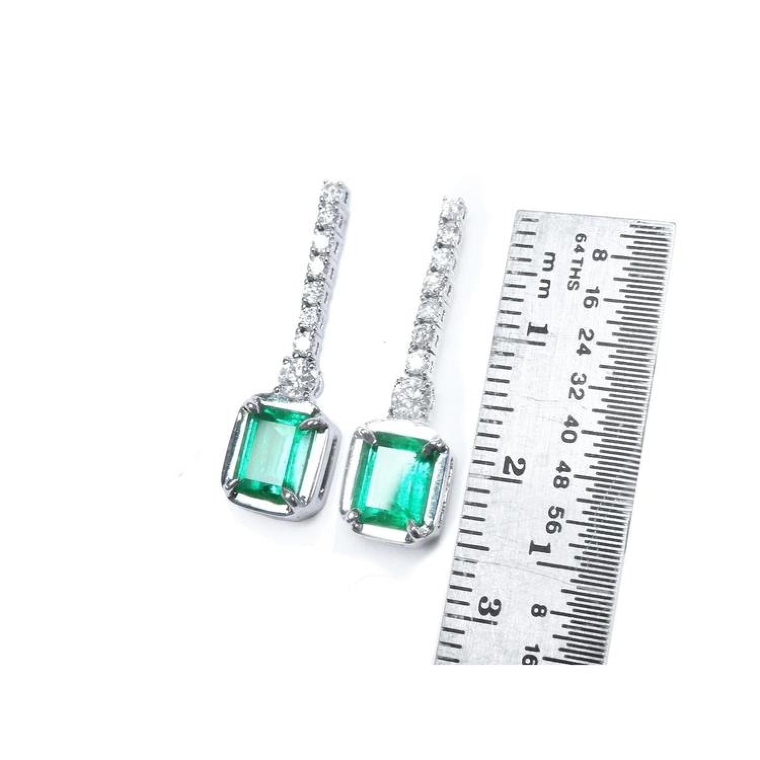 18K white gold dangling earrings with emerald-cut Colombian emeralds and diamond studs, shown with ruler.