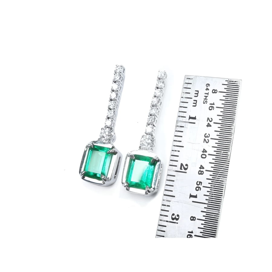 18K white gold dangling earrings with emerald-cut Colombian emeralds and diamond studs, shown with ruler.