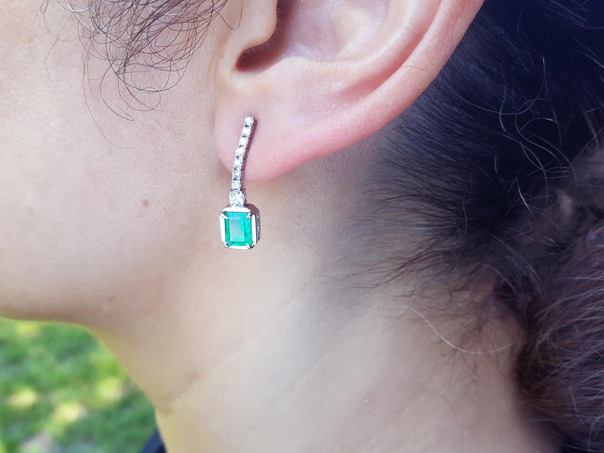 Close-up of a real Colombia emerald earring on a person&#39;s ear with a blurred natural background