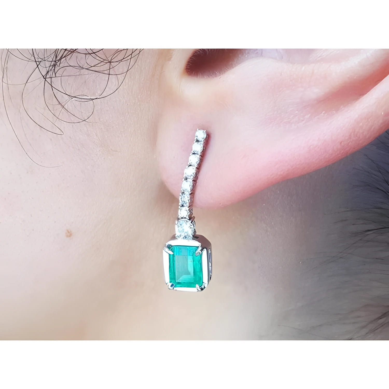 Close-up of a natural colombian  emerald dangle earring with diamonds on a person's ear.