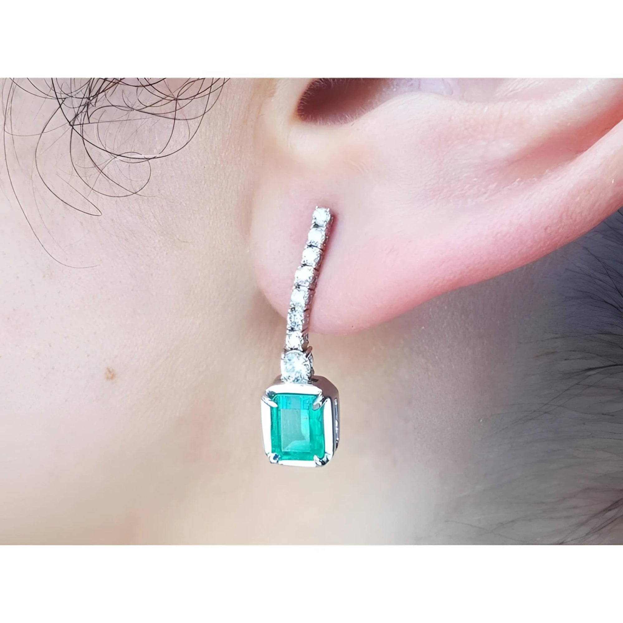 Close-up of a natural colombian  emerald dangle earring with diamonds on a person's ear.