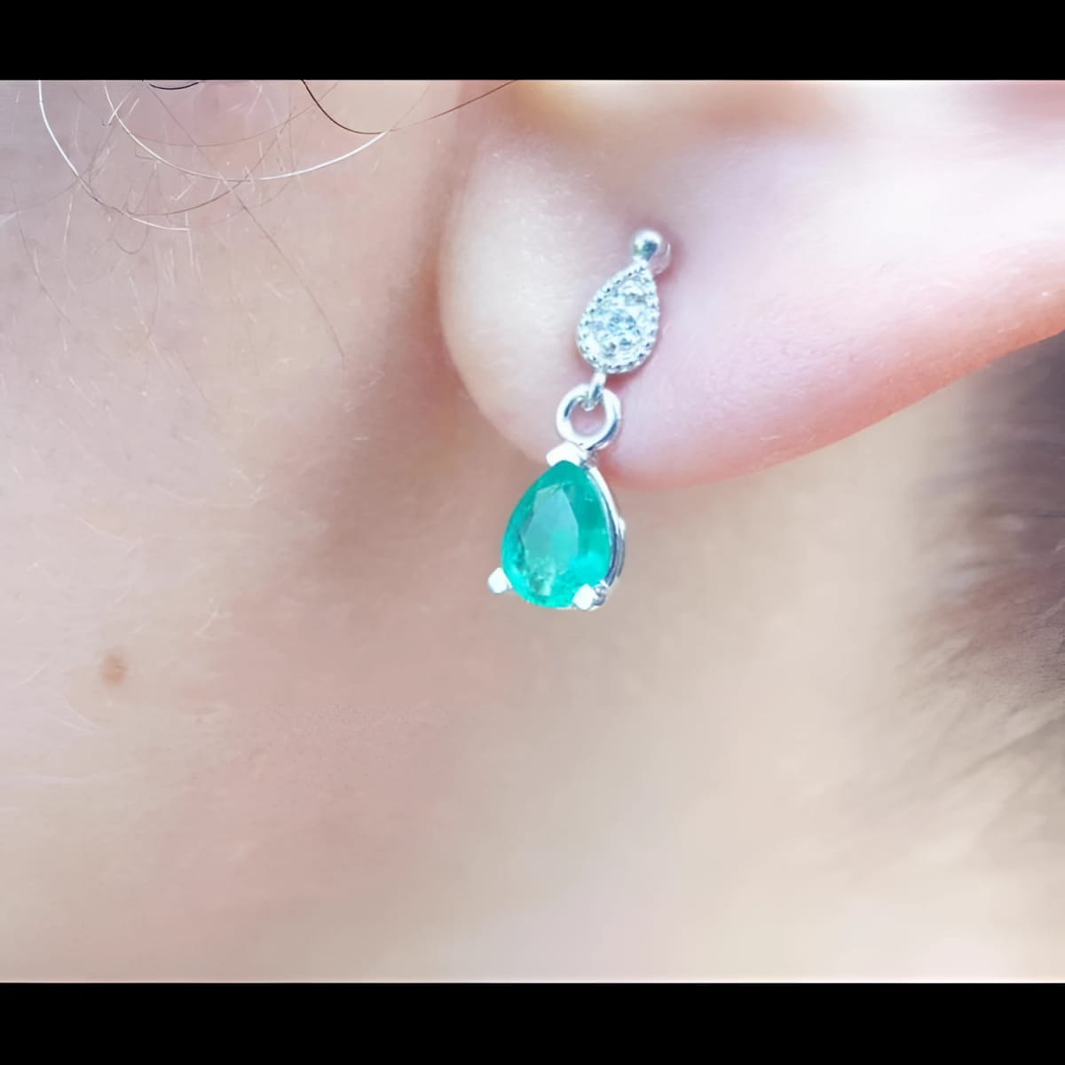 Close-up of an emerald and diamond teardrop earring in white gold on a woman's ear.