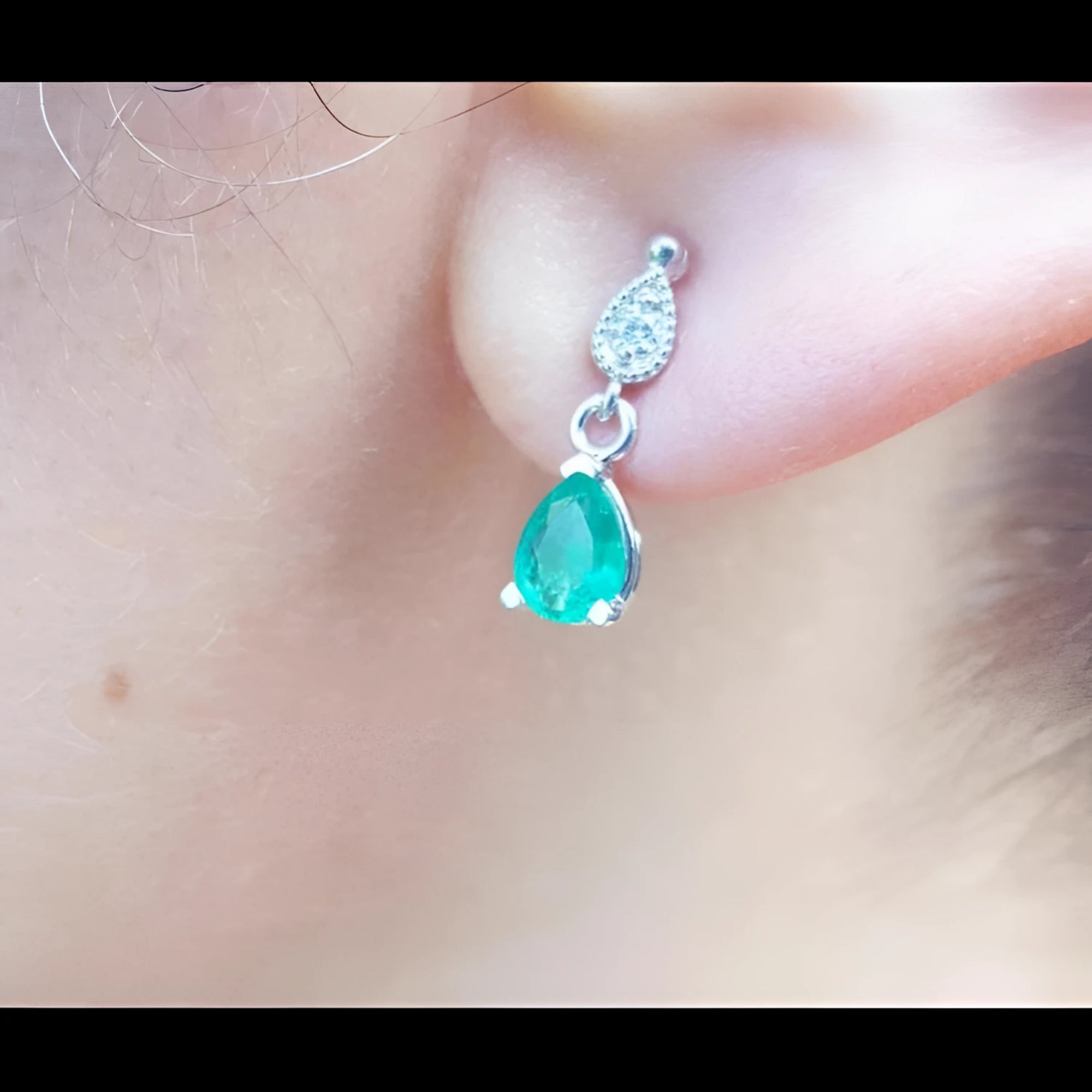 Close-up of an emerald and diamond teardrop earring in white gold on a woman's ear.