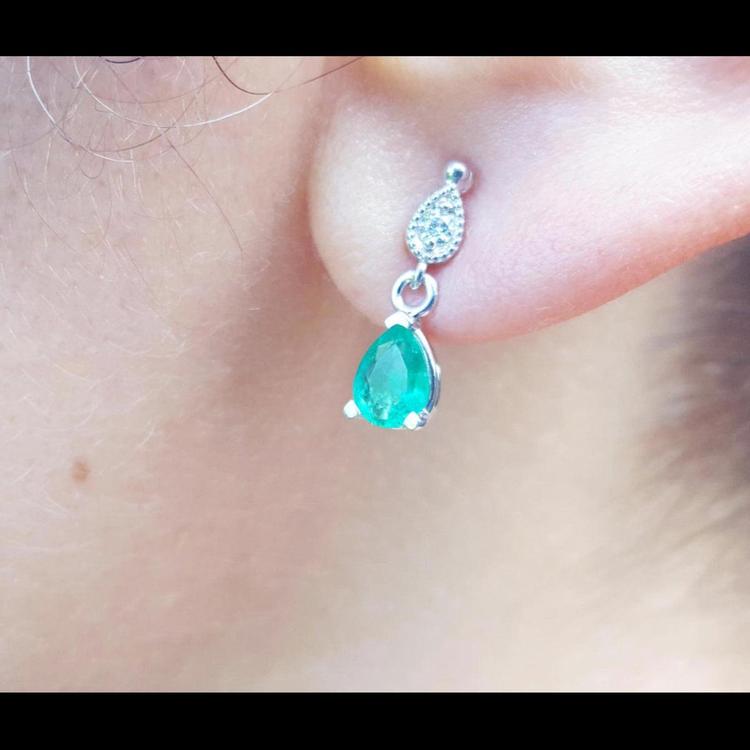Close-up of an emerald and diamond teardrop earring in white gold on a woman's ear.