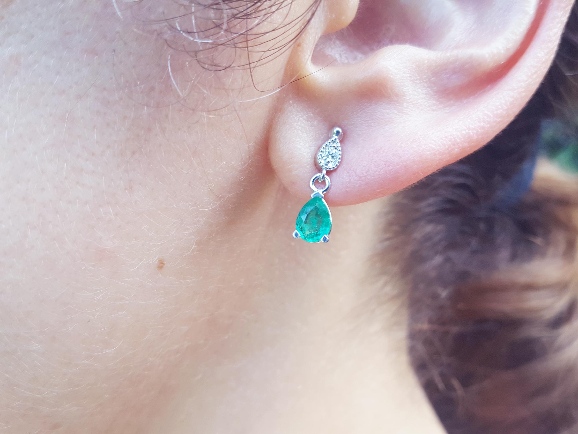 Front view of a teardrop emerald dangle earring in white gold on an earlobe
