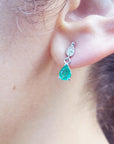Front view of a teardrop emerald dangle earring in white gold on an earlobe