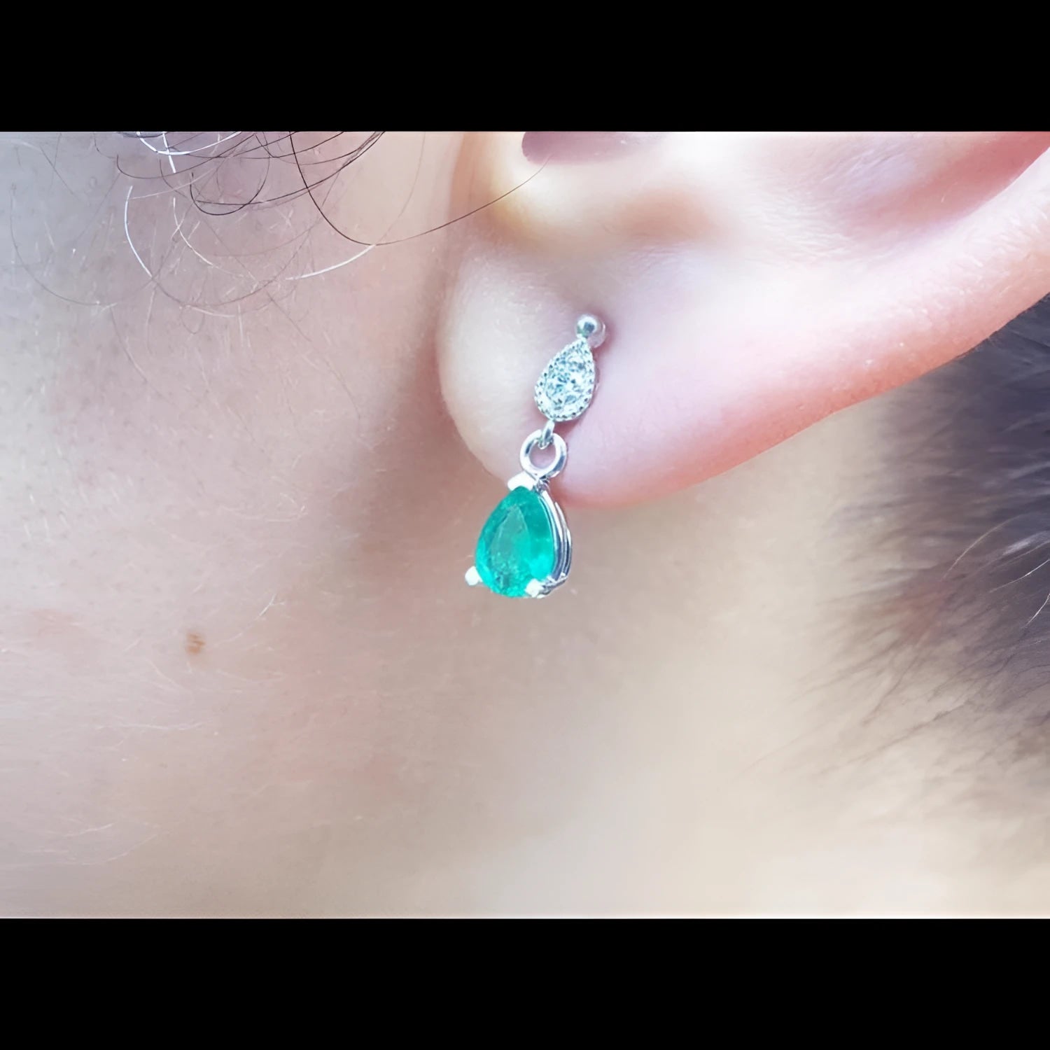 Dangling teardrop emerald earrings in 14K white gold with diamond-studded pear link on an ear.