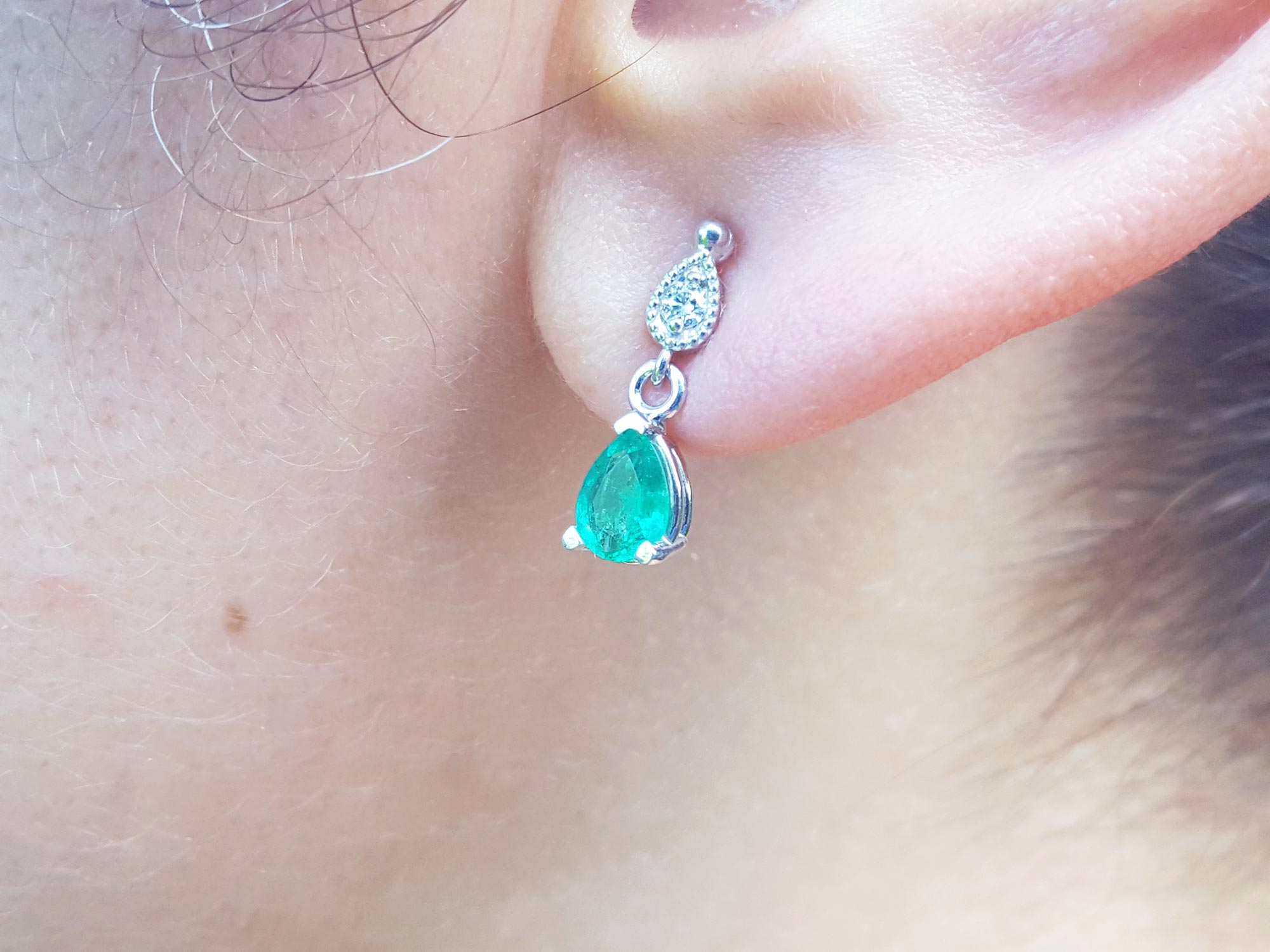 Woman&#39;s earlobe wearing a pear-cut emerald earrings left side profile