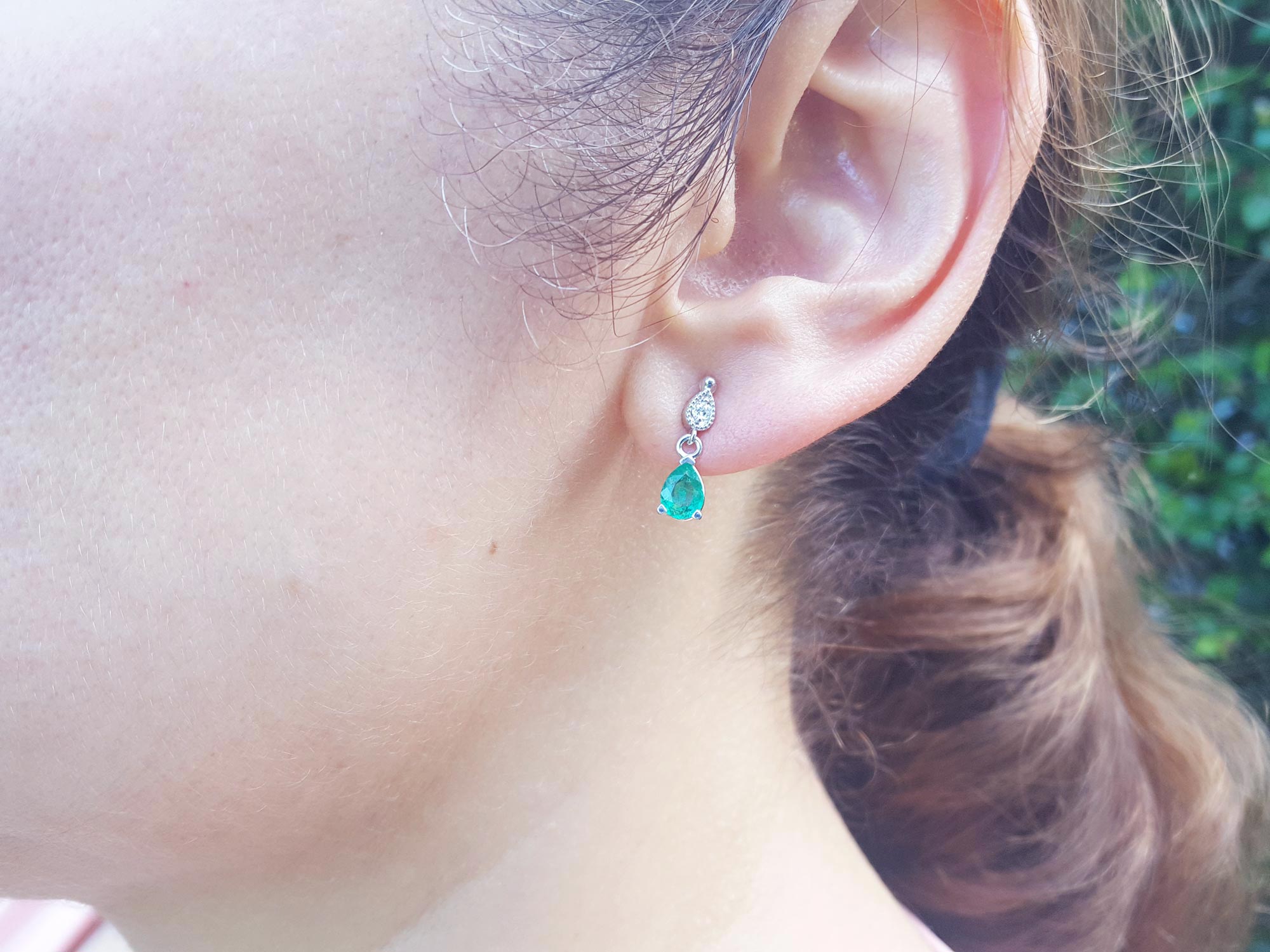 A woman&#39;s face wearing an emerald pear cut earrings on a leafy background