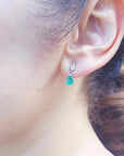 A woman's face wearing an emerald pear cut earrings on a leafy background