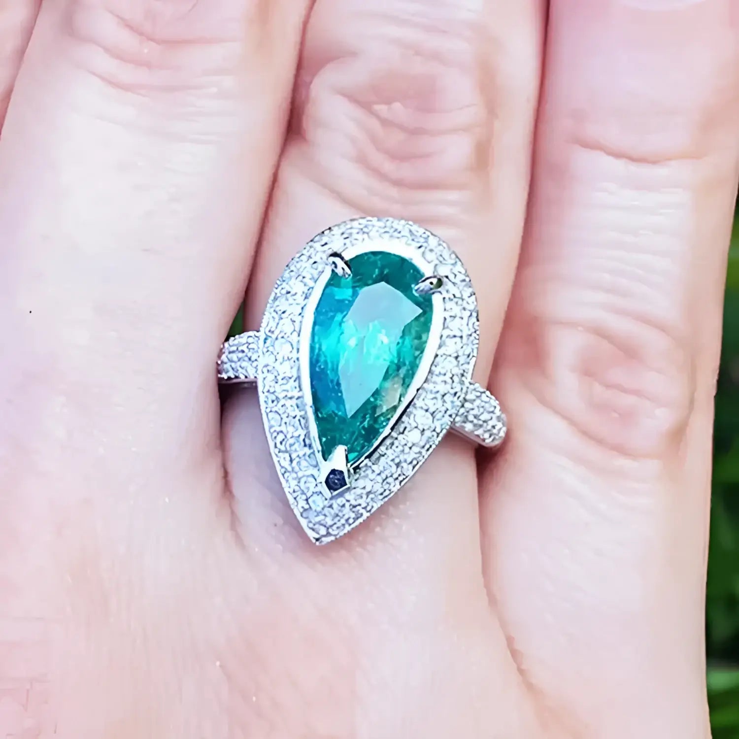 esmeralda colombiana corte pera con diamantes natural en oro blanco exhibido en una mano.