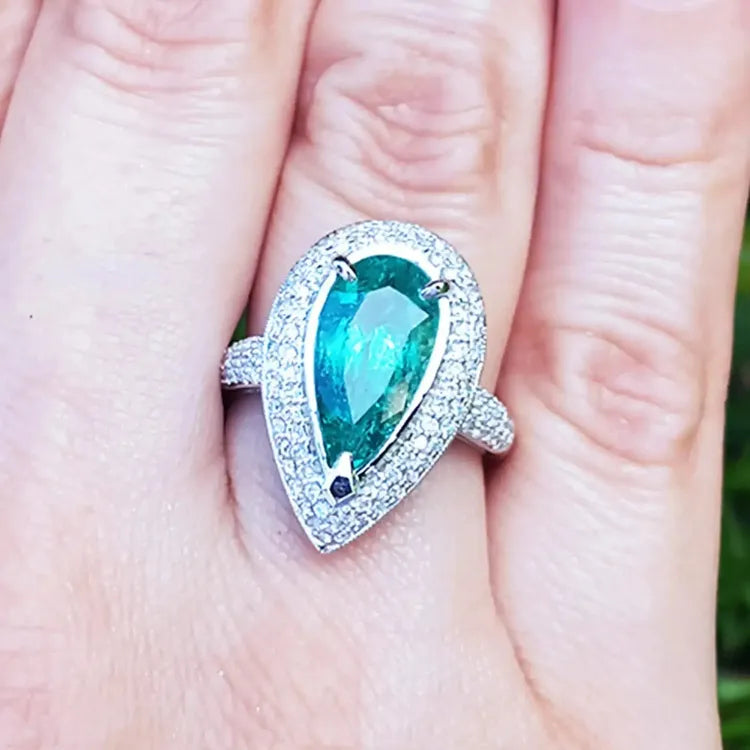 esmeralda colombiana corte pera con diamantes natural en oro blanco exhibido en una mano.