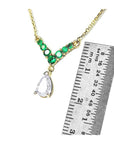 14K gold necklace with pear-cut diamond and seven round emeralds, shown with ruler for scale.