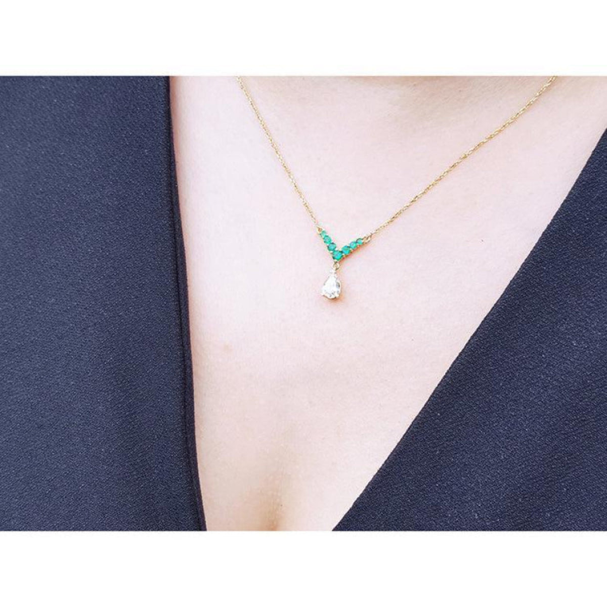 14K gold necklace with pear-cut diamond and V-shaped emerald centerpiece on a model.