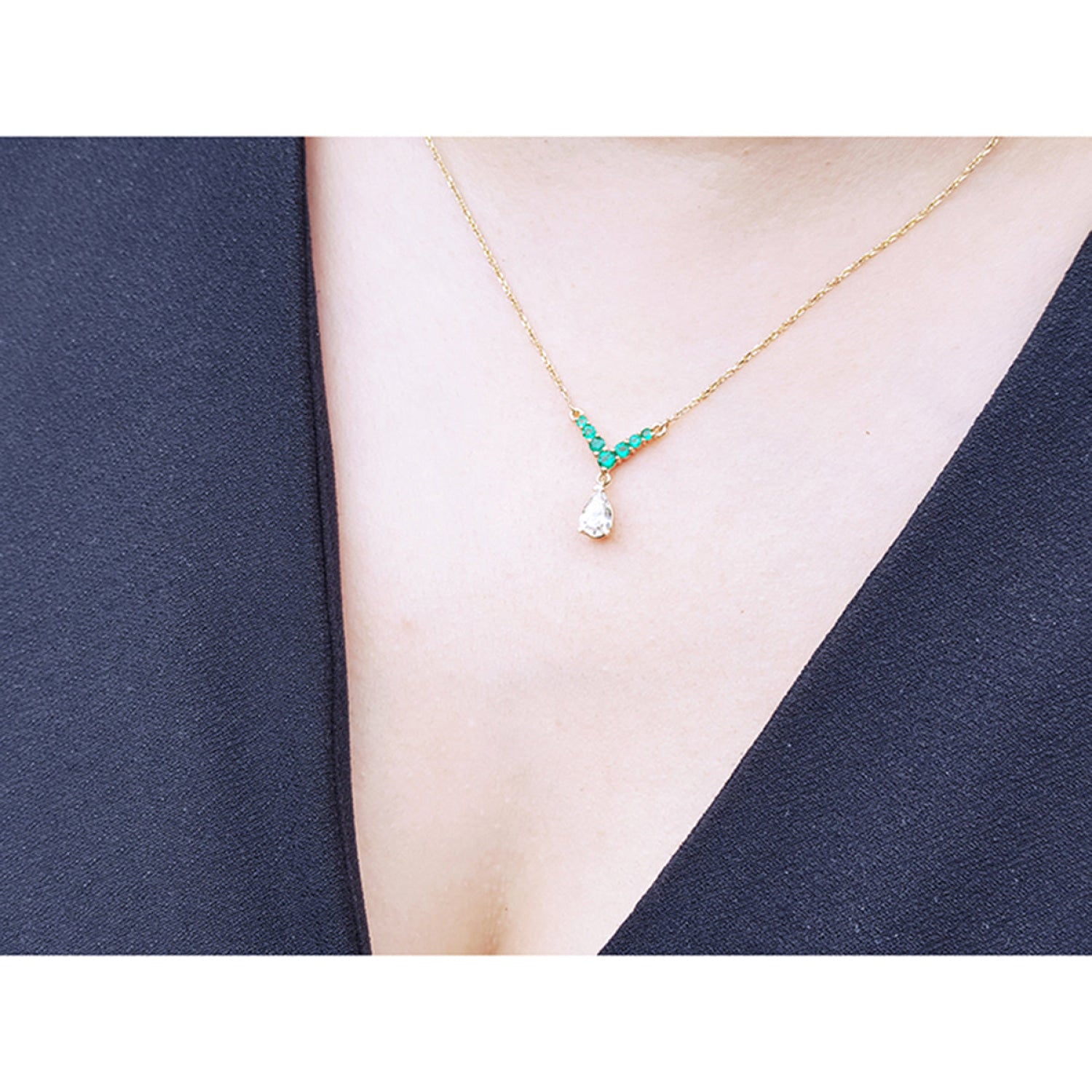 14K gold necklace with pear-cut diamond and V-shaped emerald centerpiece worn on a model's neck.