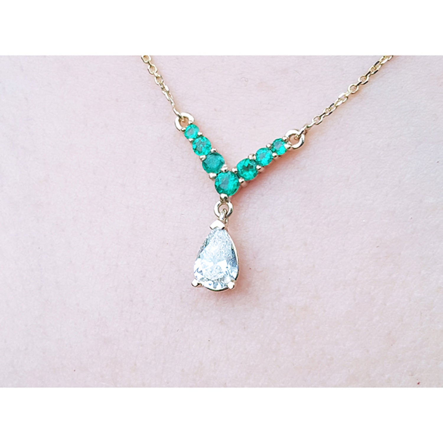 14K gold necklace with a 0.69 ct pear diamond and 0.35 ct round emeralds in a V-shape.