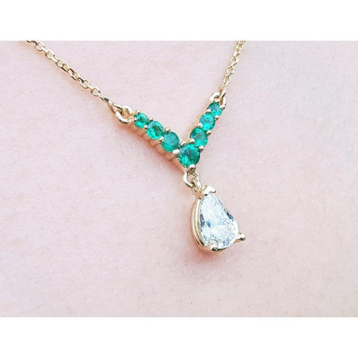 14K gold necklace with a pear-cut diamond and V-shaped emerald centerpiece.