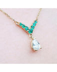 14K gold necklace with a pear-cut diamond and V-shaped emerald centerpiece.