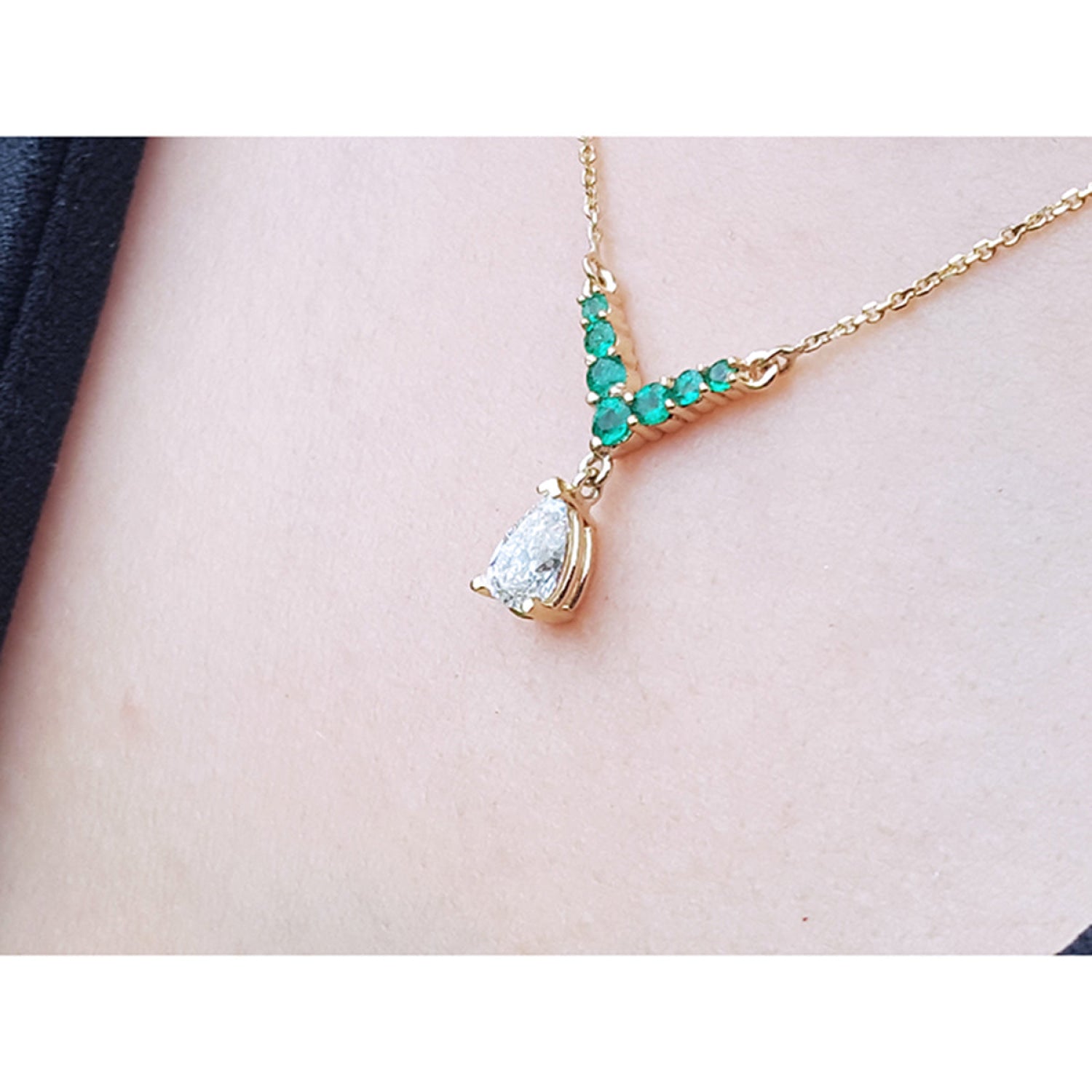  14K gold necklace with a pear-cut diamond pendant and V-shaped emerald centerpiece, shown worn on a person's neck.