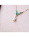 14K gold necklace with a pear-cut diamond pendant and V-shaped emerald centerpiece.