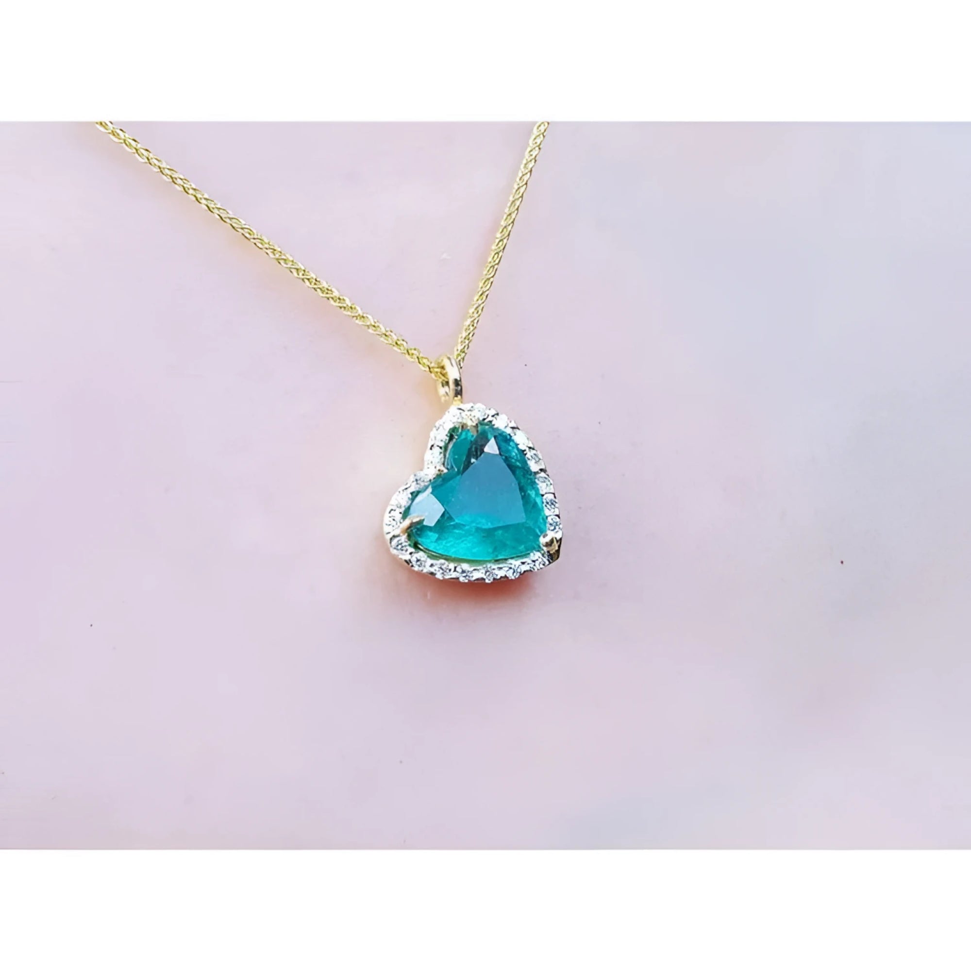 Tilted heart emerald pendant with halo diamonds on an 18K yellow gold chain.