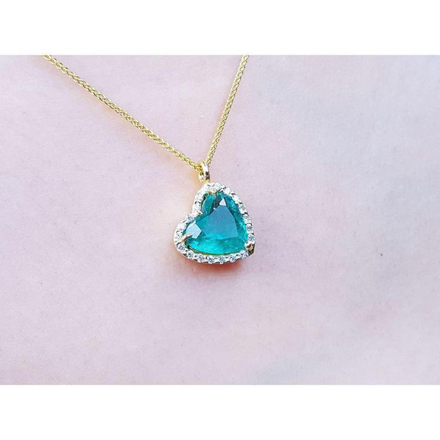 Tilted heart emerald pendant with halo diamonds on an 18K yellow gold chain.