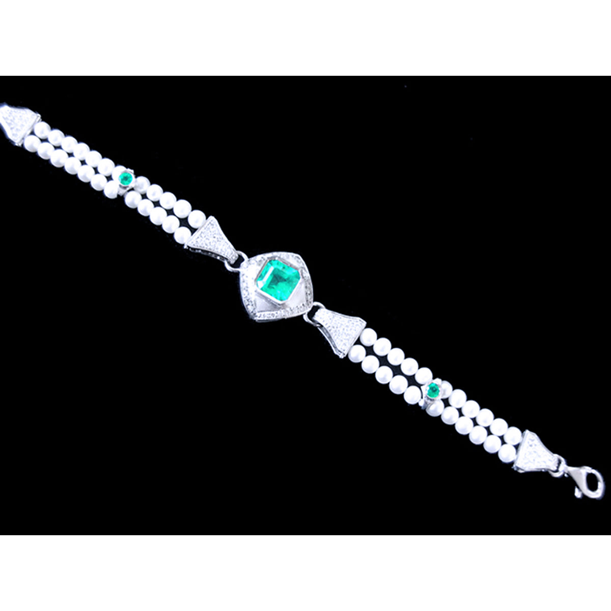A distant view of a white gold and pearls bracelet with emeralds gemstones on a black background.
