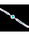 A distant view of a white gold and pearls bracelet with emeralds gemstones on a black background.