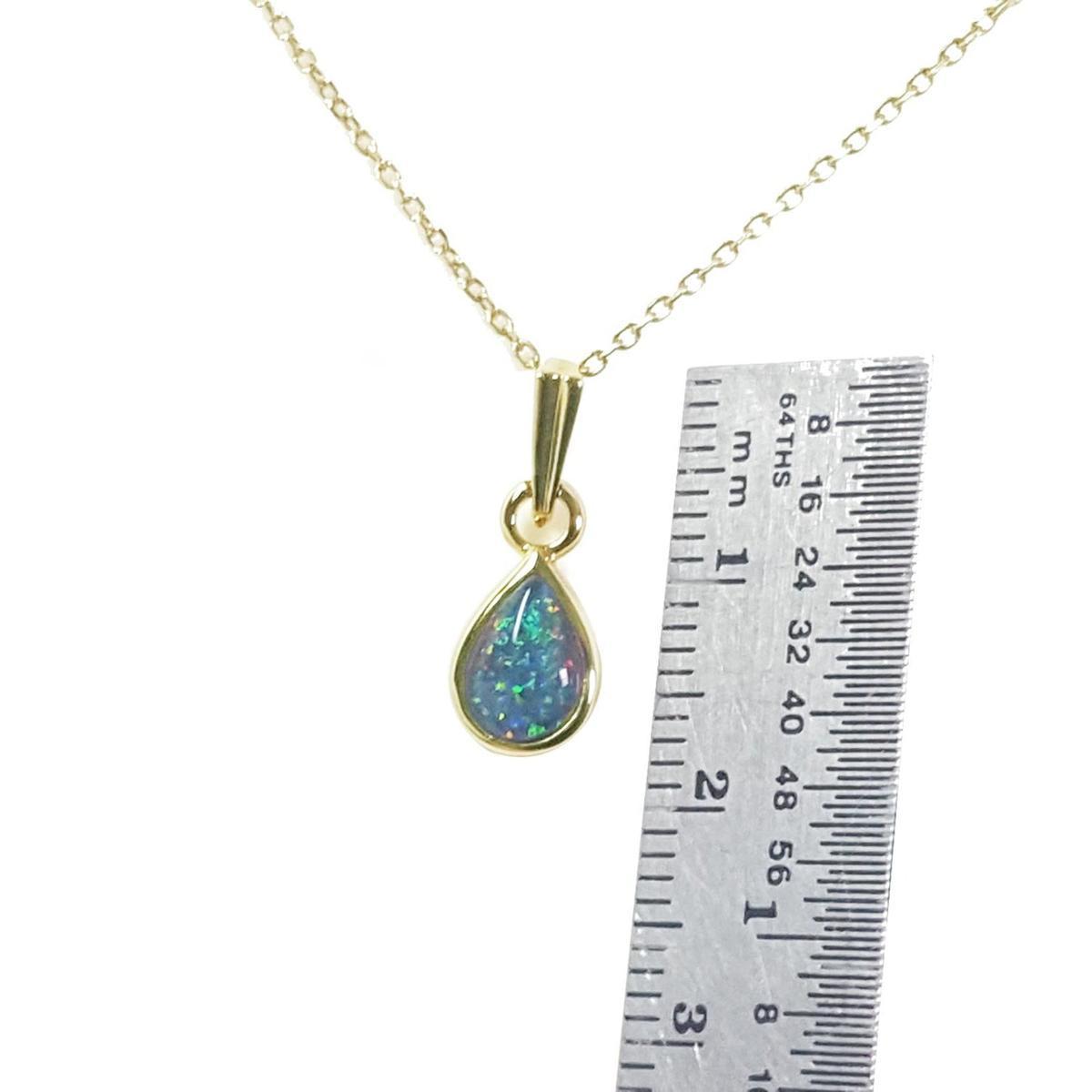 Gold necklace with a teardrop-shaped opal pendant next to a ruler for scale on a white background.