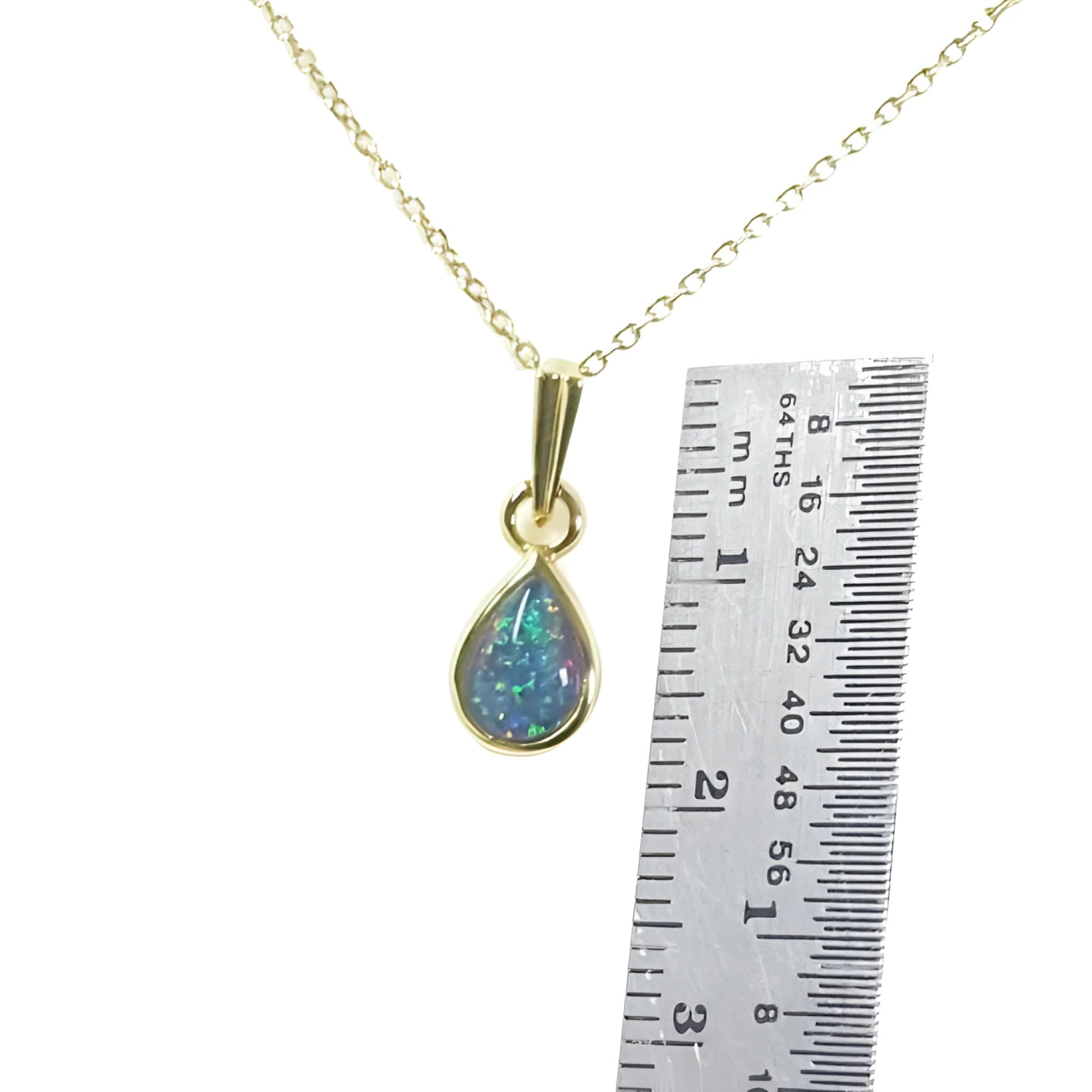 Pear-shaped doublet opal pendant with bluish-green sparkle, bezel set in 14K yellow gold on a chain, next to a ruler.