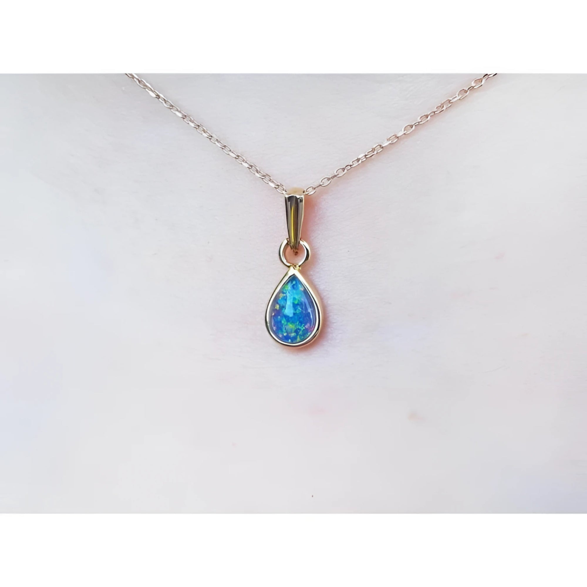 Pear-shaped Australian doublet opal pendant with bluish-green sparkle, bezel set in 14K yellow gold on a chain.