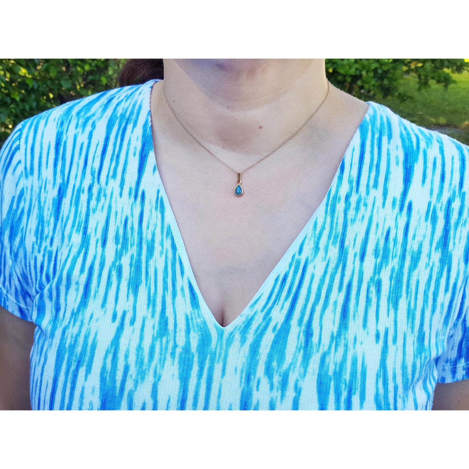 A woman wearing a blue and white patterned top with a necklace featuring a blue opal pendant.