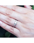 14K white gold engagement ring with a round center diamond and trillion side diamonds on a hand.