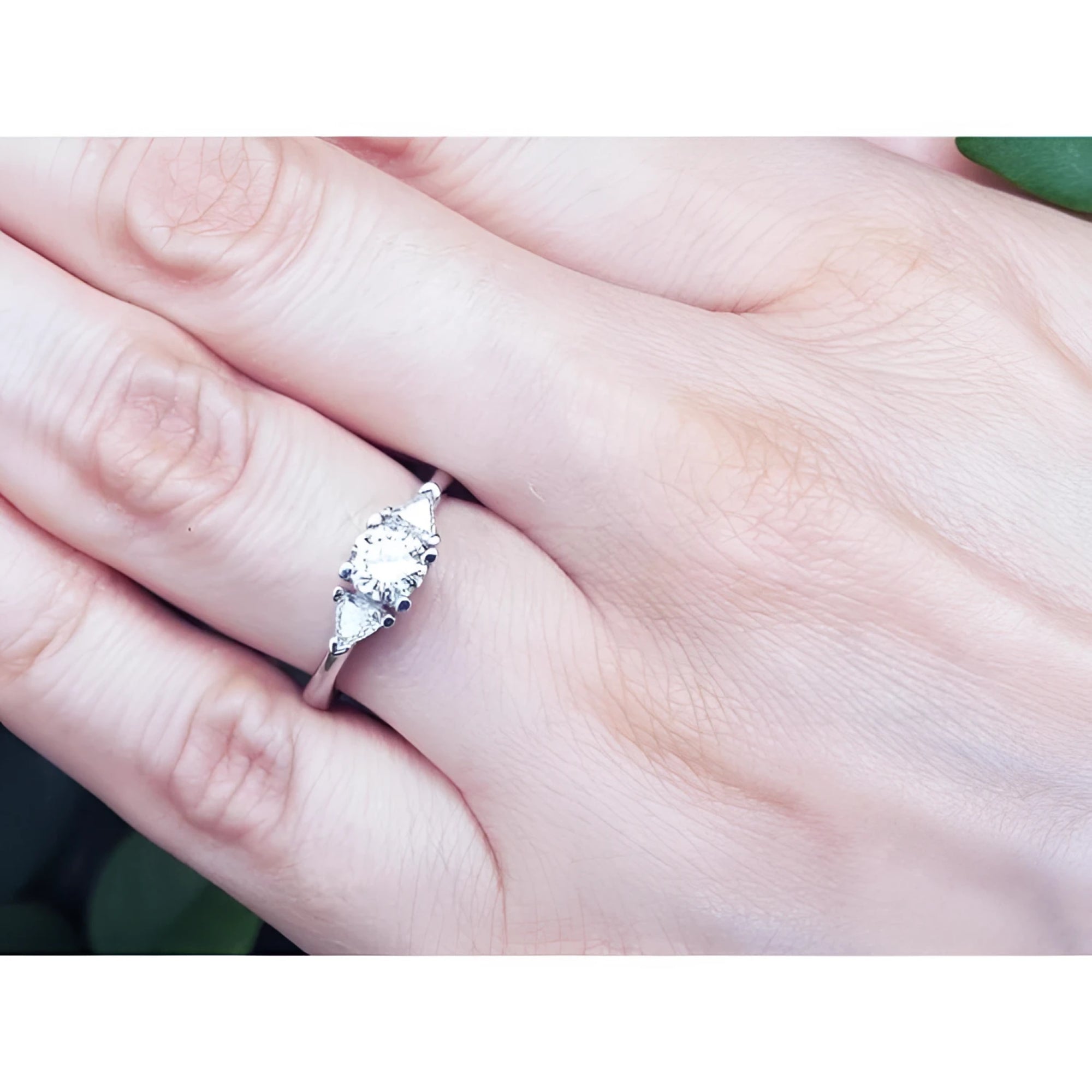 14K white gold engagement ring with a round center diamond and two trillion side diamonds on a hand.