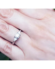 14K white gold engagement ring with a round center diamond and two trillion side diamonds on a hand.