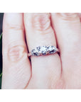 14K white gold three-stone round cut diamond engagement ring with pave accent diamonds on a hand.