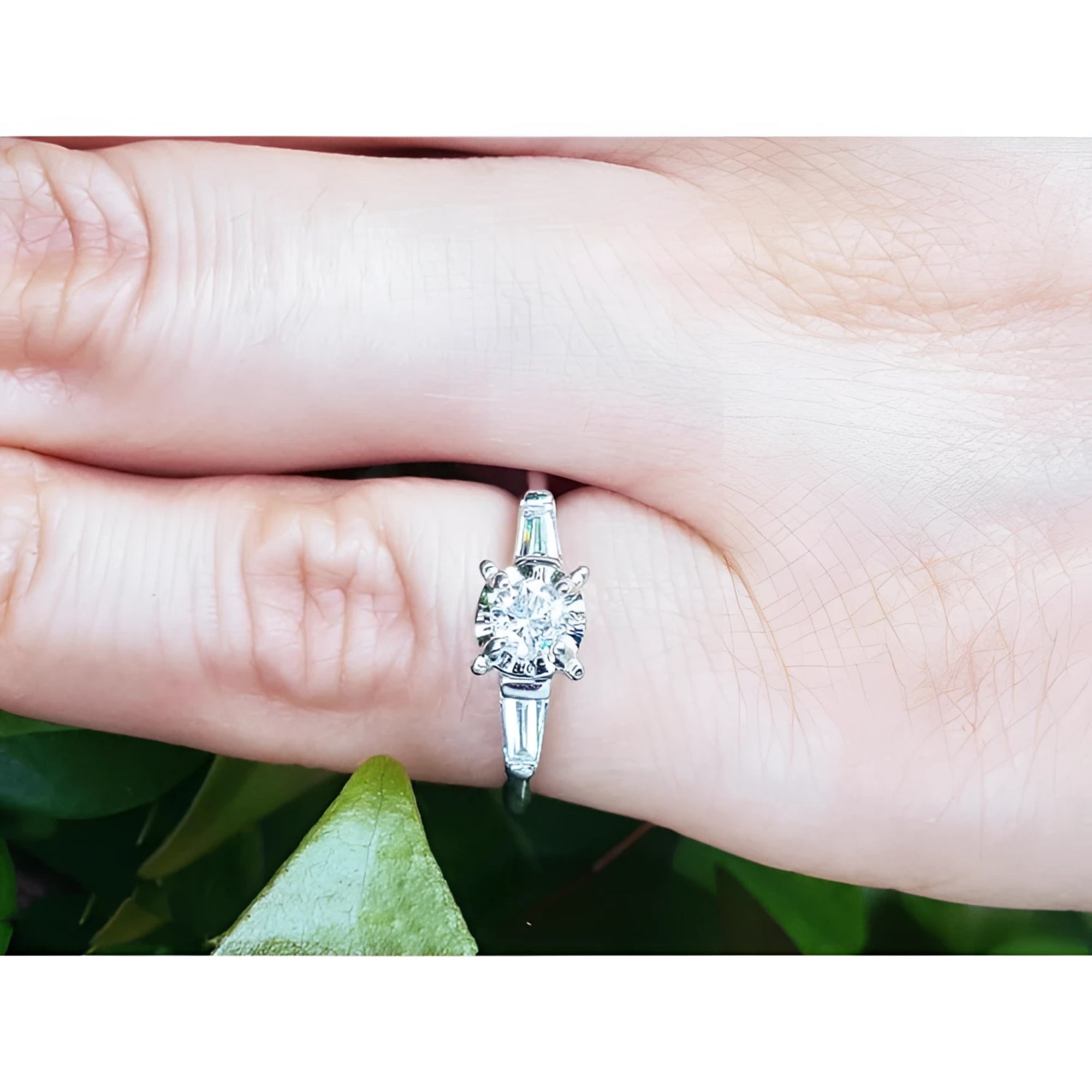 14k white gold engagement ring with round diamond and baguette side stones on a finger.