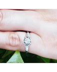 14k white gold engagement ring with round diamond and baguette side stones on a finger.