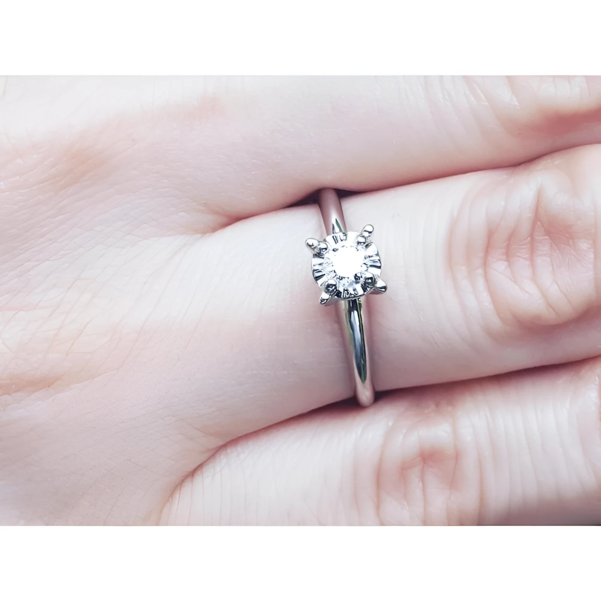 Round cut diamond solitaire engagement ring in 14K white gold, worn on a finger.
