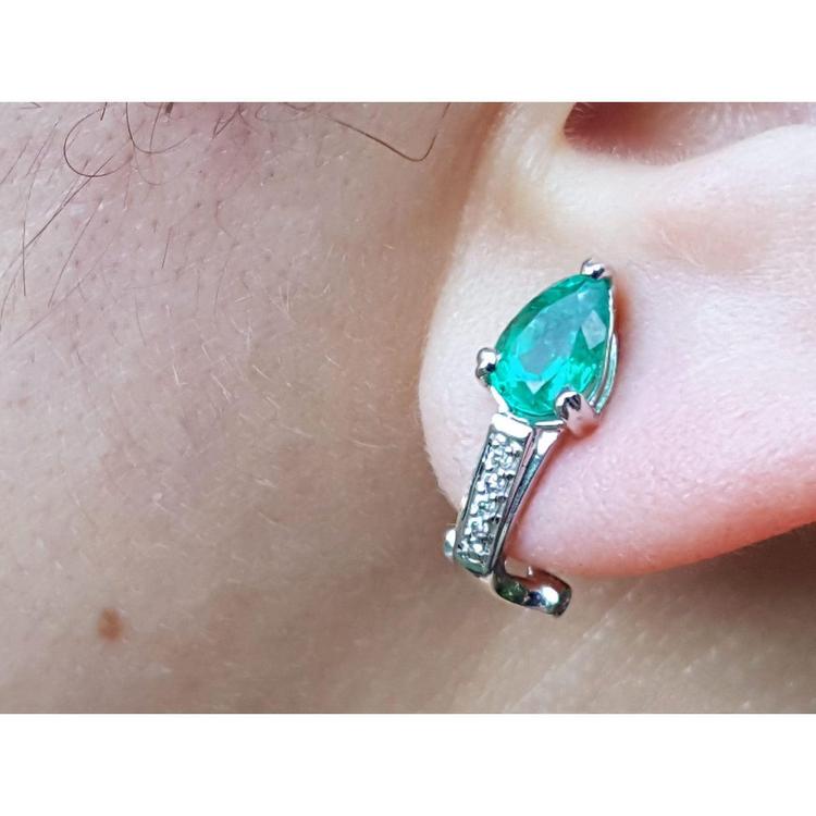 Close-up of a teardrop emerald earring clip-on system on an ear.